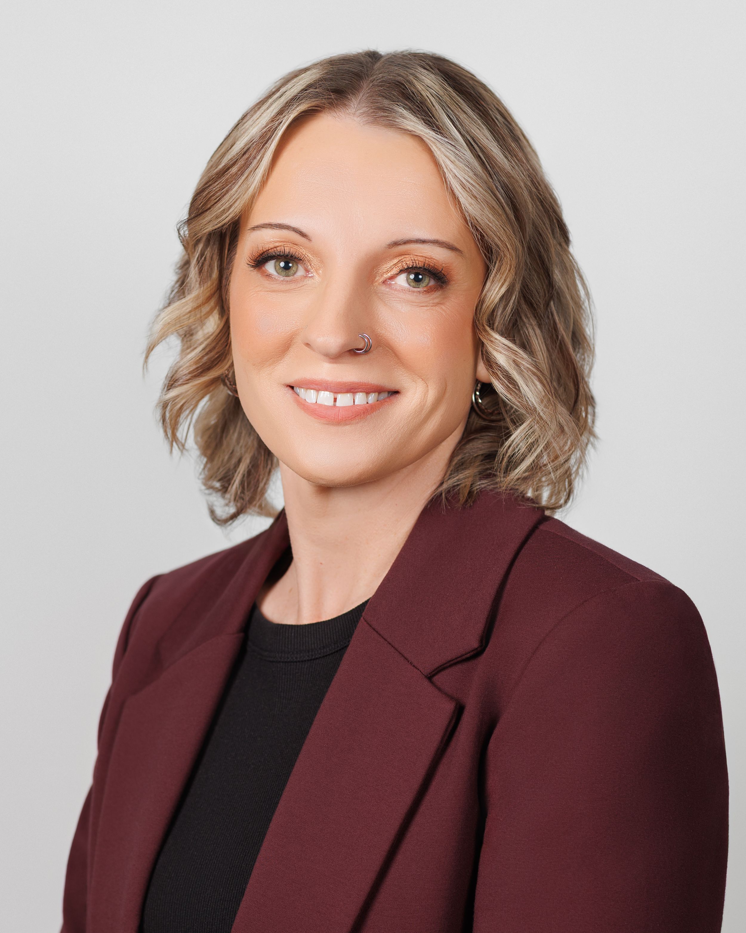 Professional headshot portrait showing a warm smile and burgundy blazer against a light gray background.