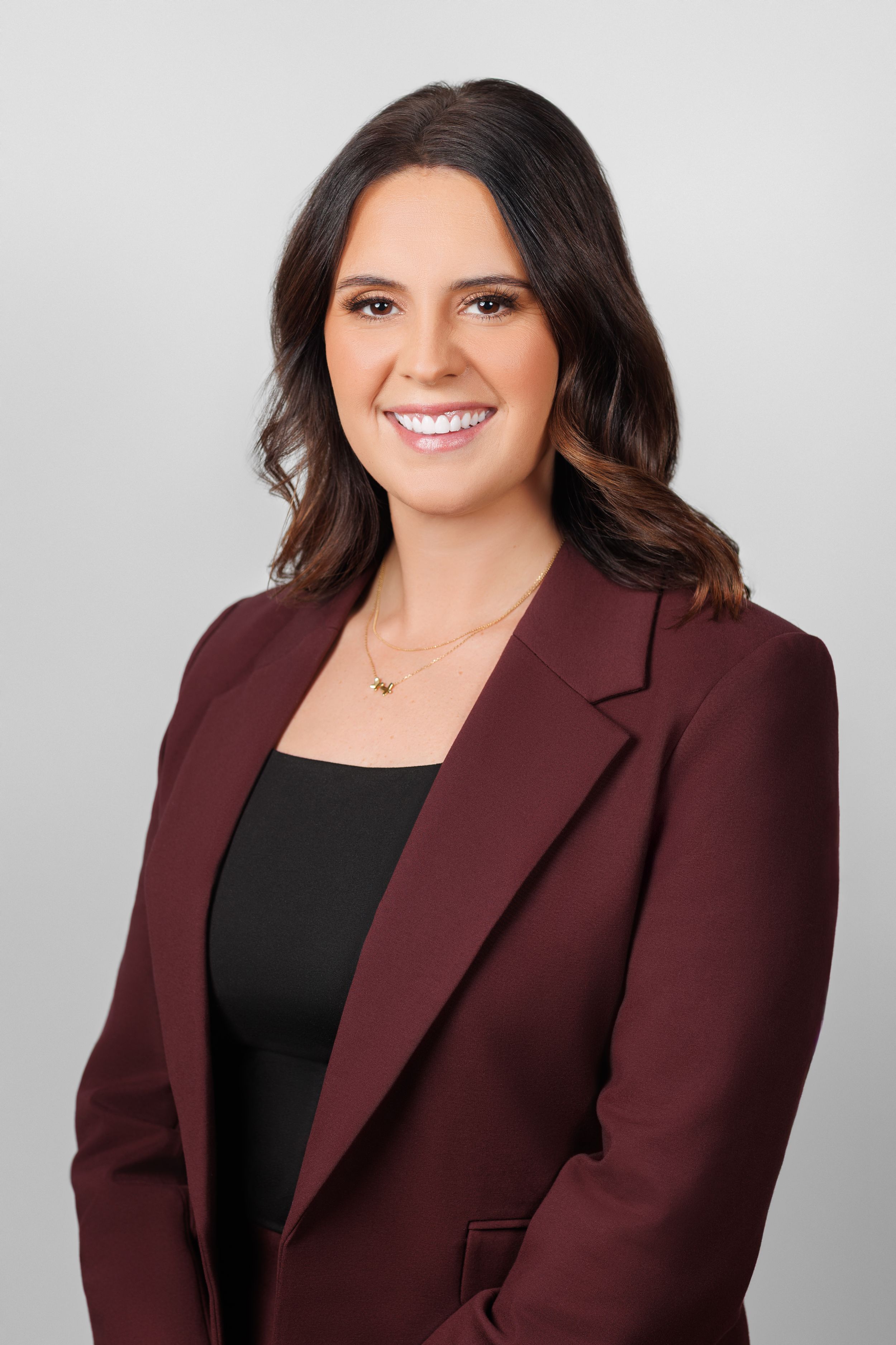 Business portrait of someone wearing a maroon blazer and black top with a confident expression.