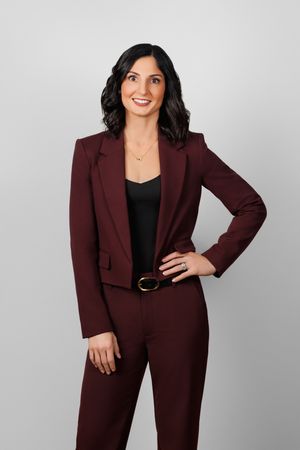 Professional portrait of someone wearing a burgundy business suit with black top against a gray background.