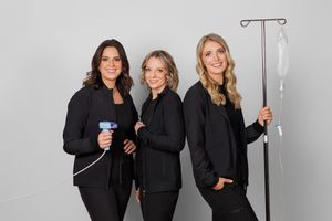 Three women in black business attire pose together against a light gray background.