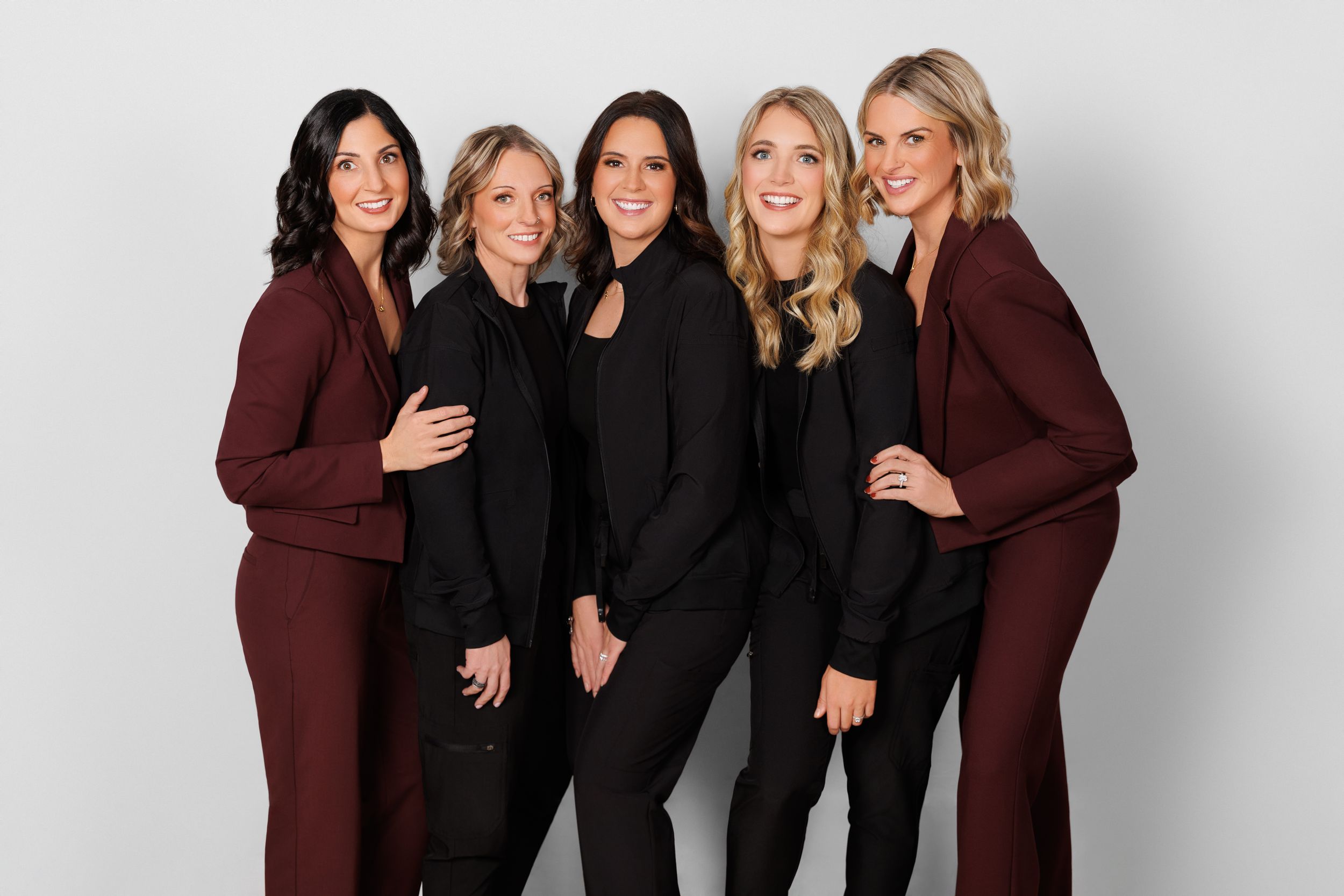 A group of women posing together wearing coordinated black and burgundy outfits in a studio setting.