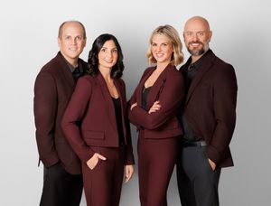Professional group photo of people wearing coordinated burgundy and brown business attire against a light gray background.