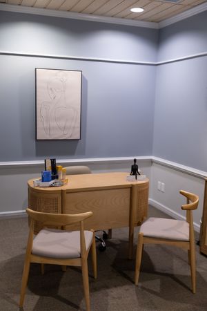 Modern office space with wooden desk, chairs, and blue-gray walls in a minimalist setting.