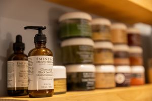 Row of natural skincare products and essential oil bottles arranged on wooden shelf with soft lighting.