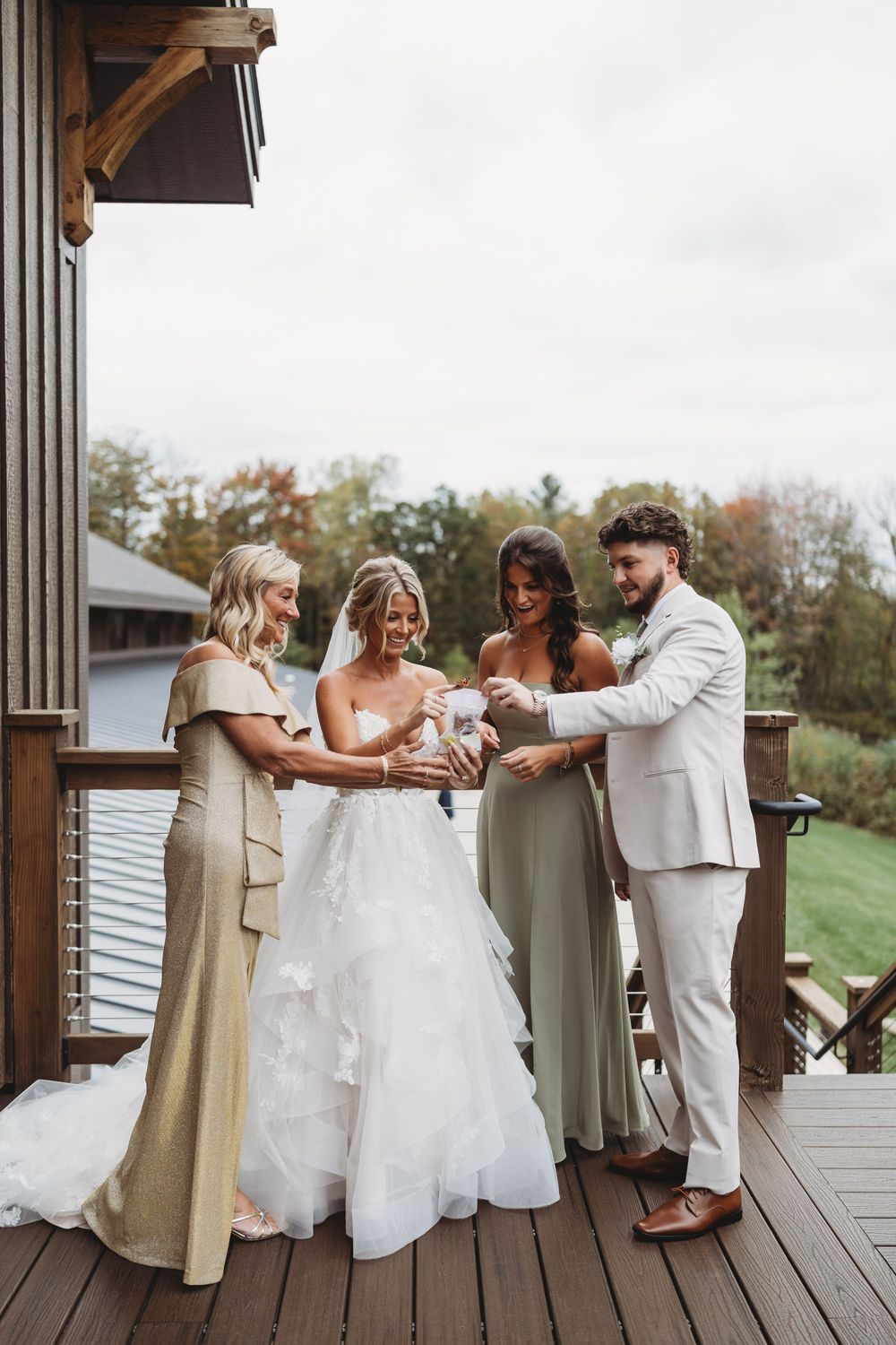 Wedding party laughs and dances together on a wooden deck during a joyful celebration.