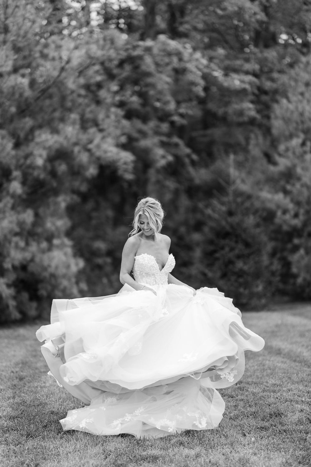 A bride in a flowing white wedding dress twirls gracefully on a grassy lawn creating a beautiful circular motion effect.