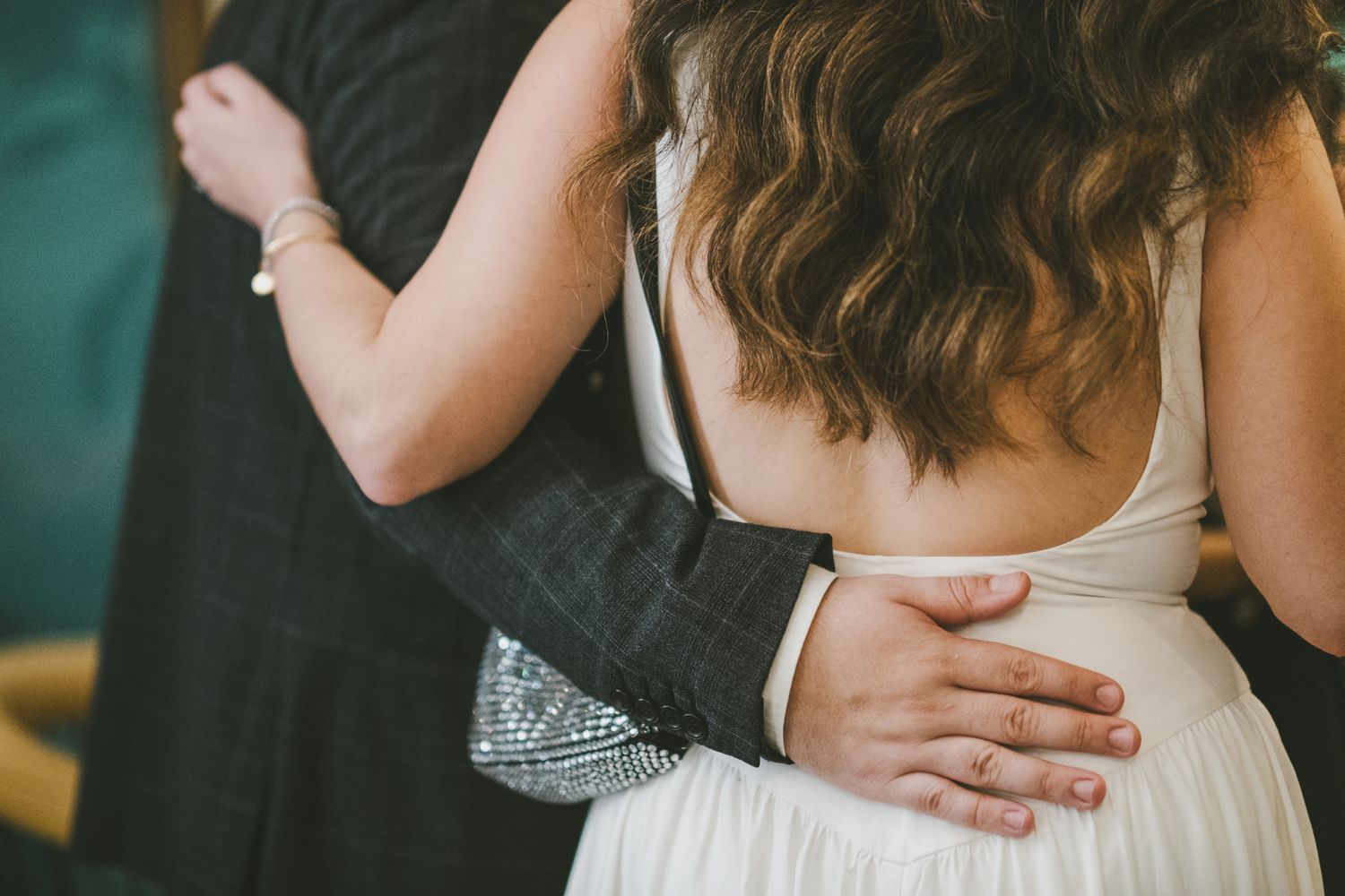 Close-up shot of a couple embracing at a wedding, with hands on white dress and black suit visible.