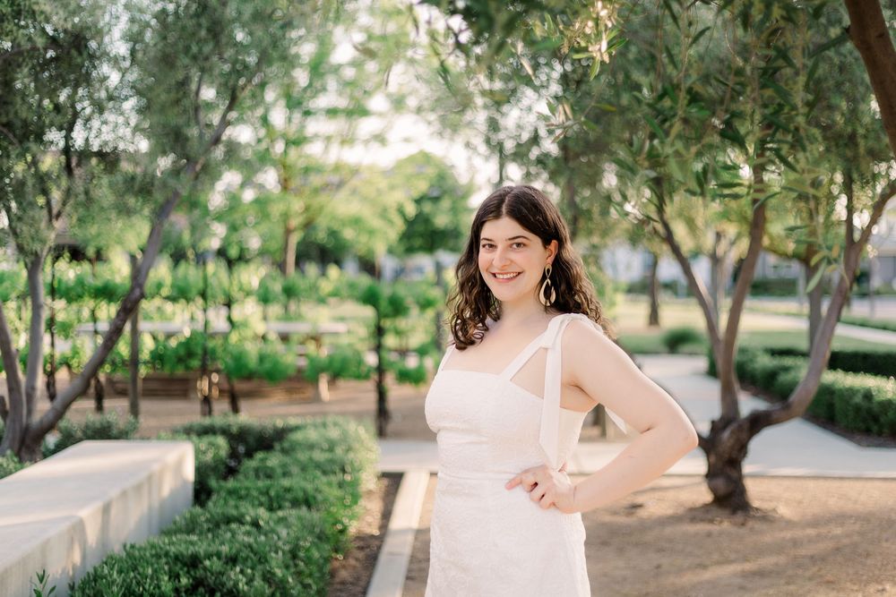 A woman in a flowing pink dress twirls gracefully in a sunlit garden setting.