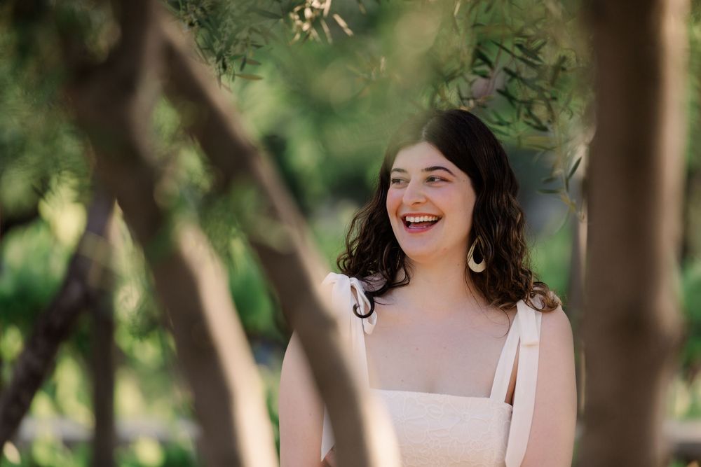 A joyful moment captured outdoors with natural greenery and sunlight filtering through trees in the background.