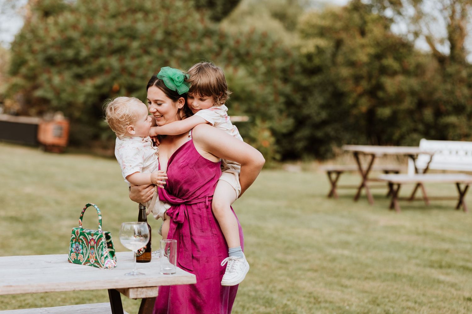 Outdoor wedding celebration with people dancing and embracing on a sunny lawn with picnic tables in the background.