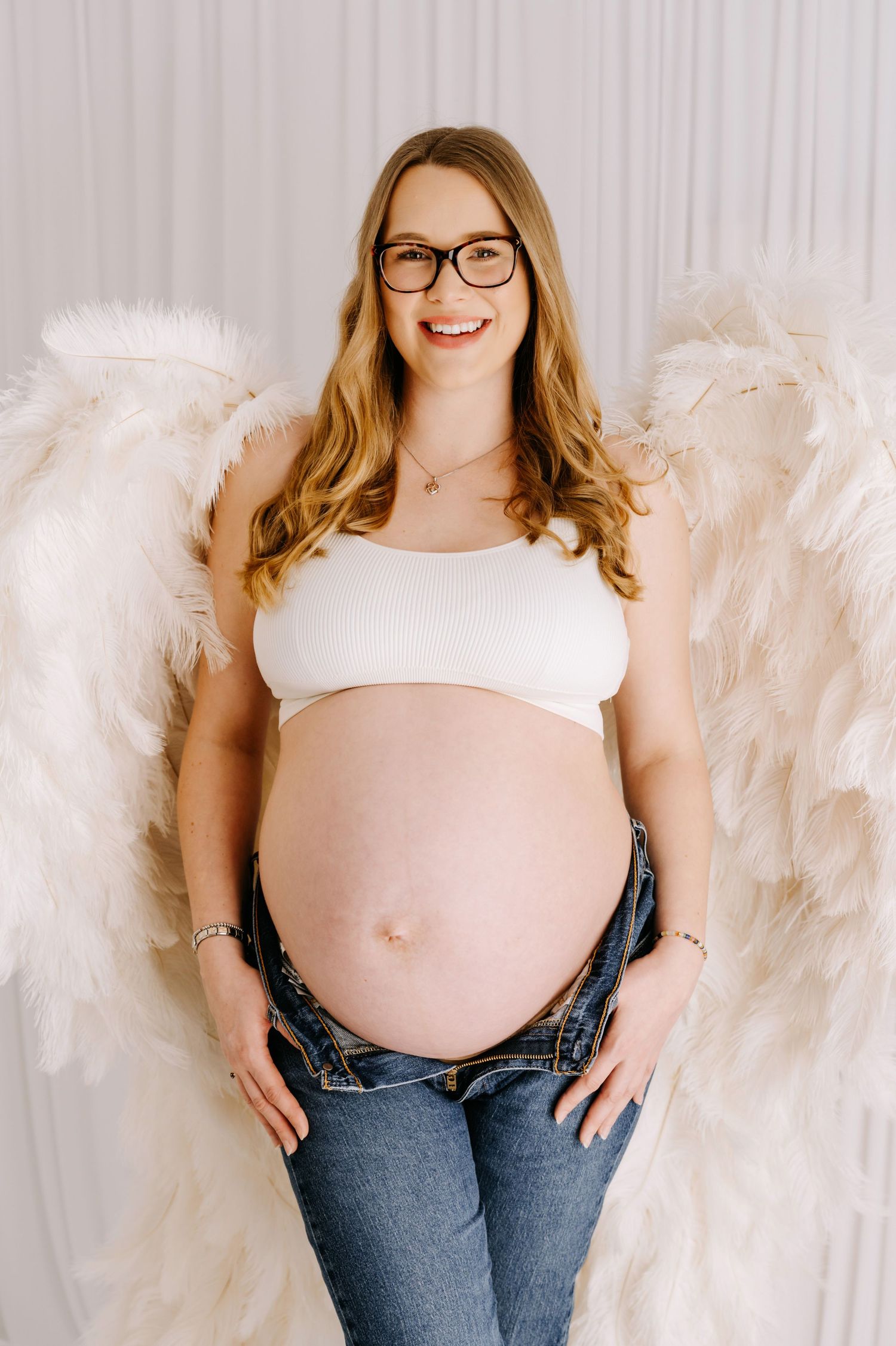 Maternity photo series showing couple in white attire against grey backdrop in romantic intimate poses.