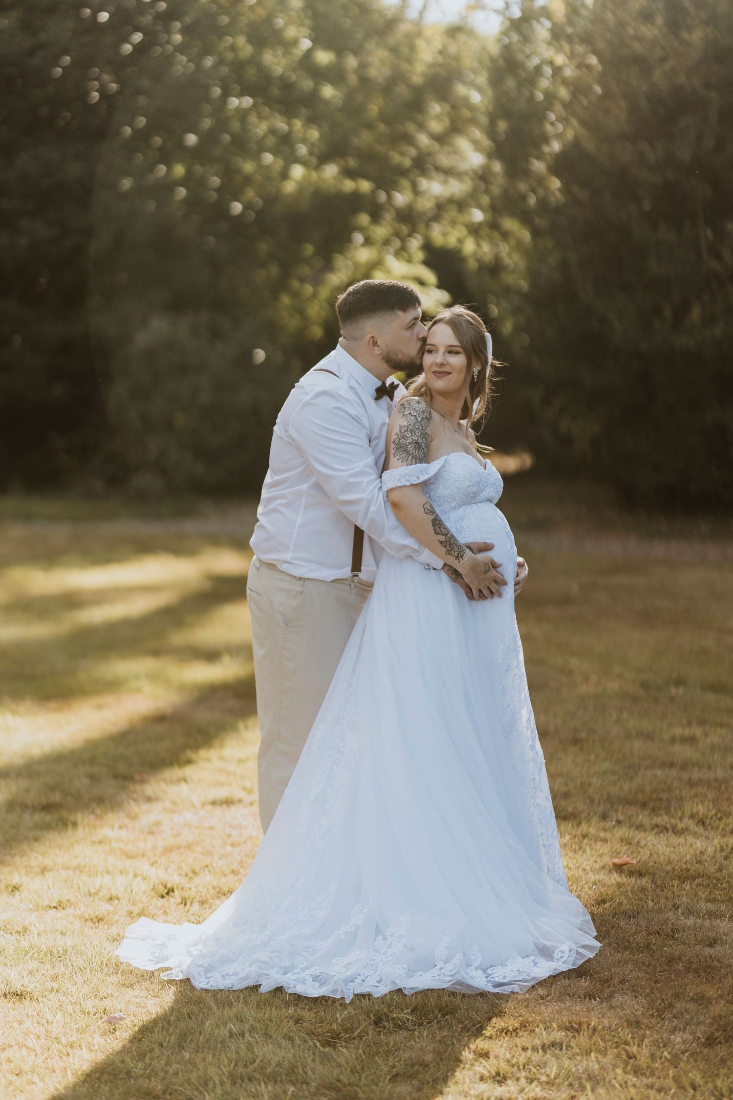 A romantic wedding couple embraces in a sunlit field during golden hour, the bride wearing a flowing white lace gown.