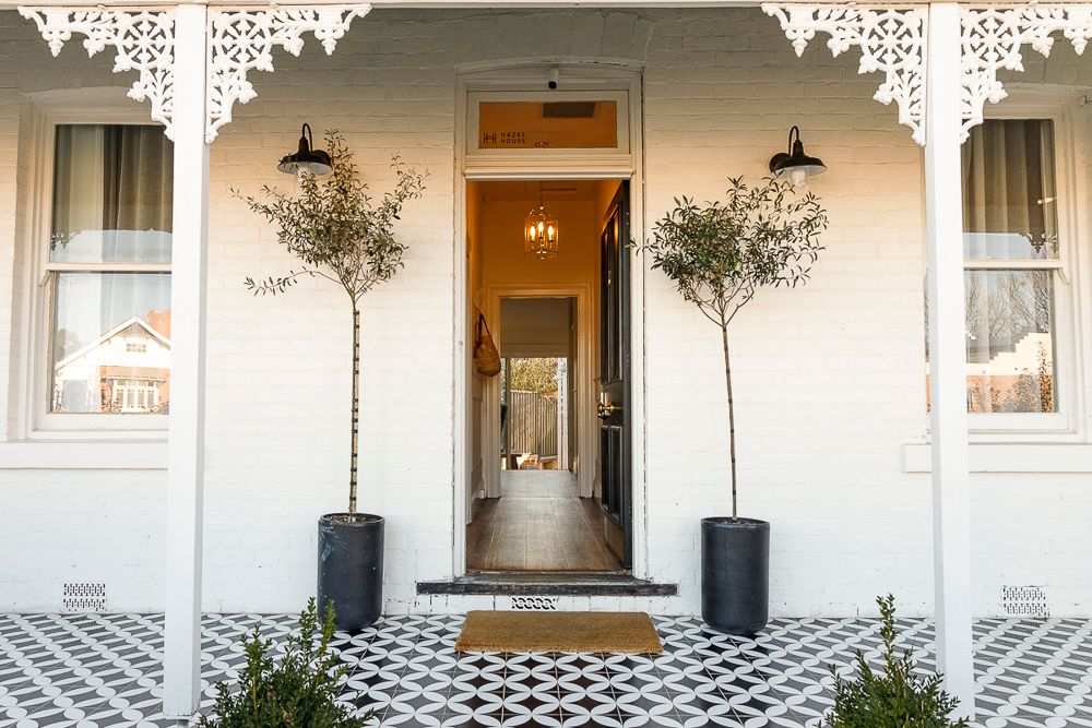 Property photo by Em Callaghan, exterior of a historic cottage with white walls, iron lacework, black and white tiles and a timber hallway.
