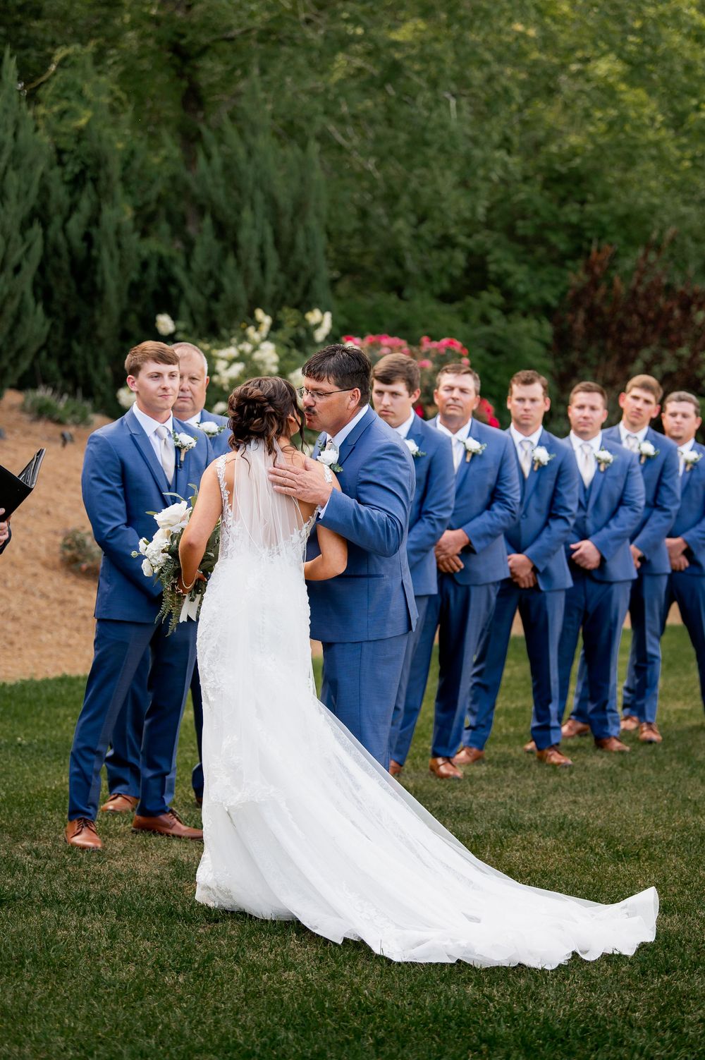 Wedding party lines up in blue suits and white gown for outdoor portrait session.