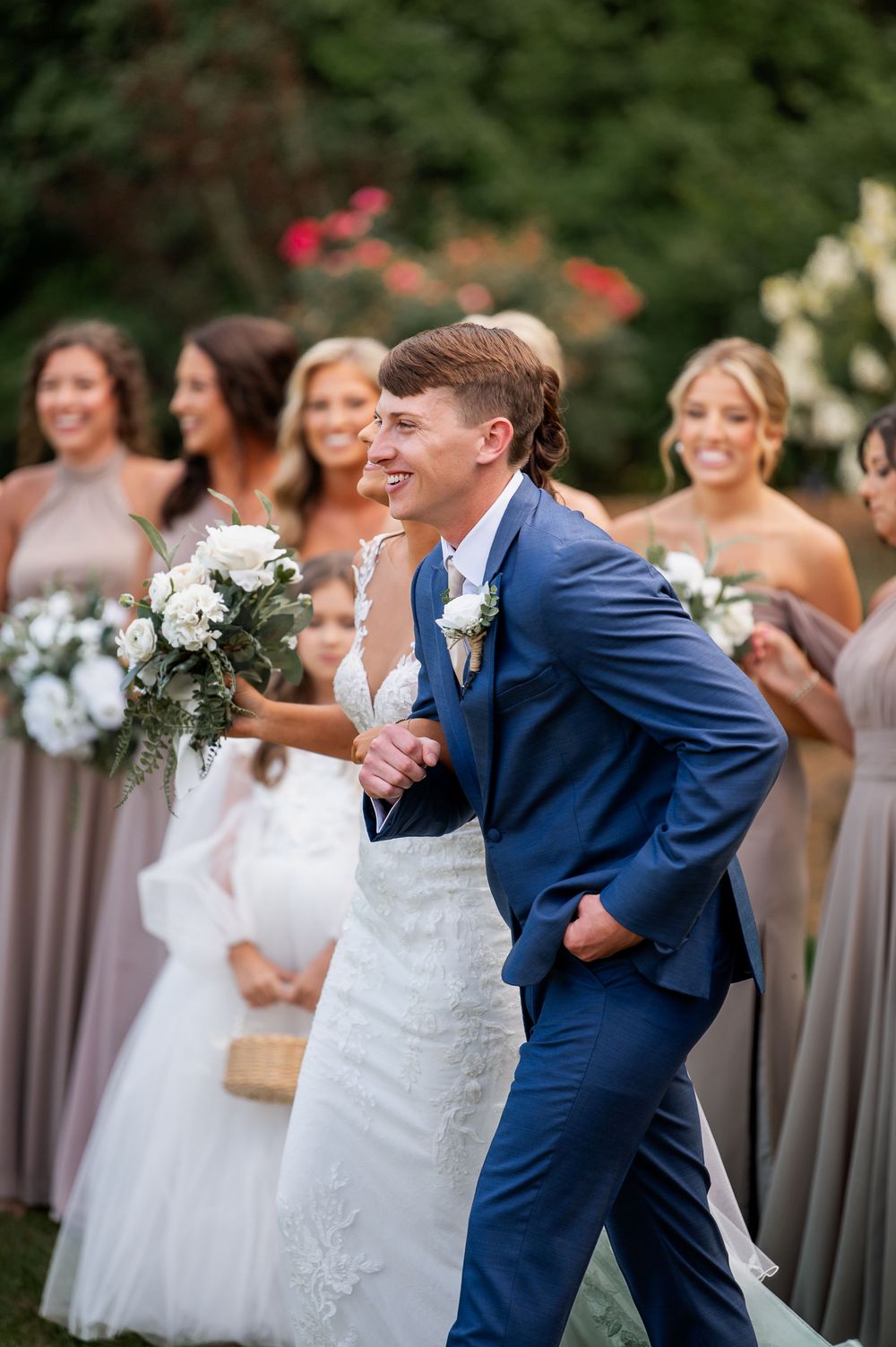 Wedding party celebrates joyfully on lawn with bridesmaids in mauve dresses.