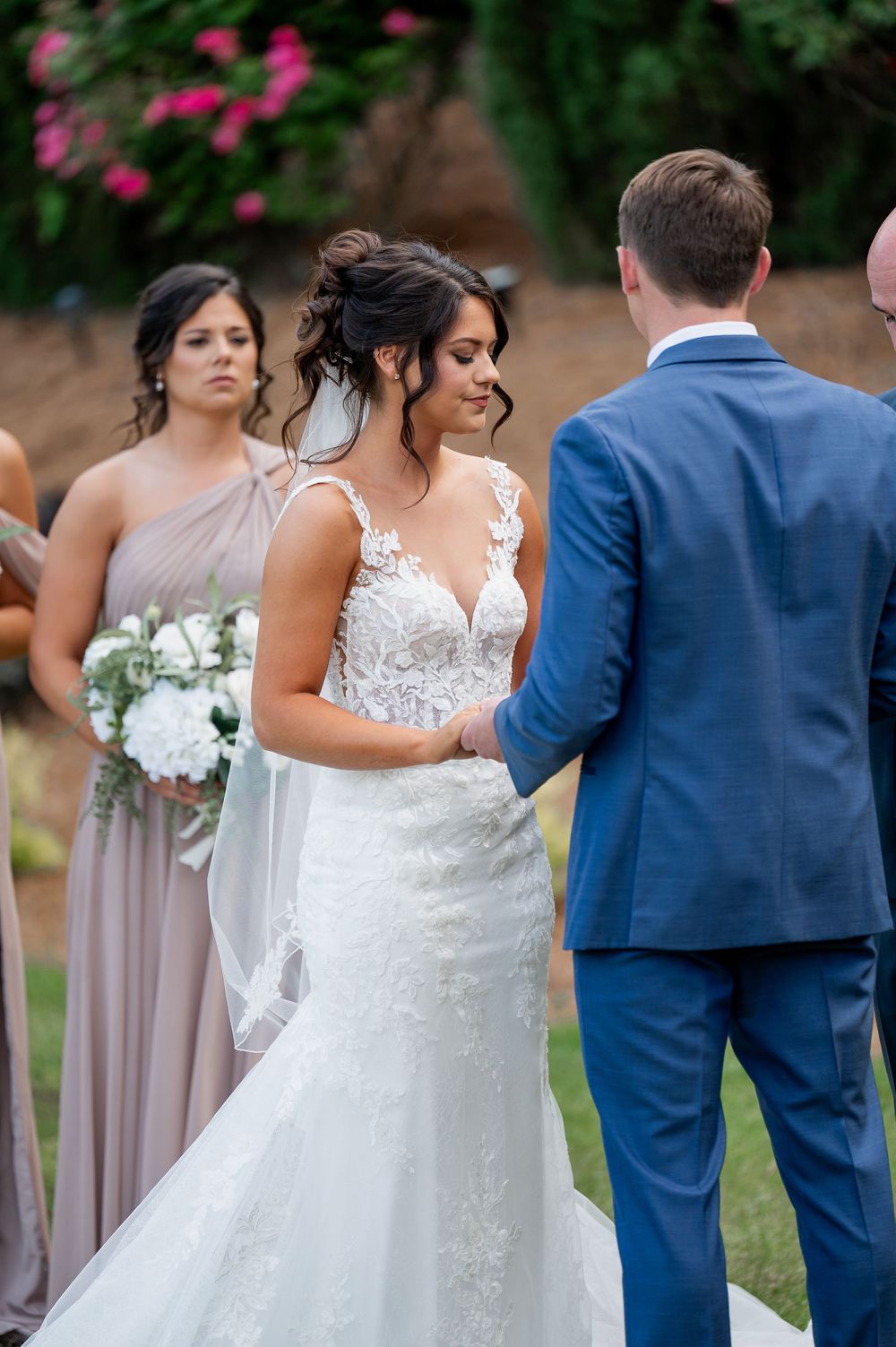 Wedding party members in blue suits and blush dresses pose during outdoor celebration.