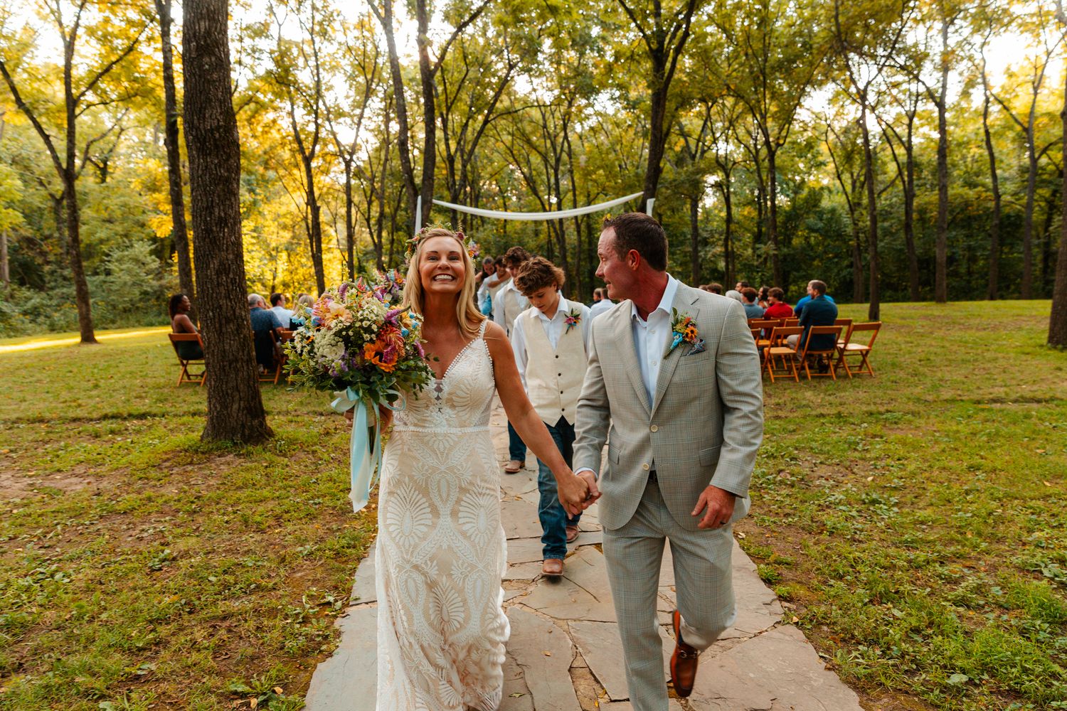Wedding party members walking and celebrating on a tree-lined path during golden hour. wedding photography st louis