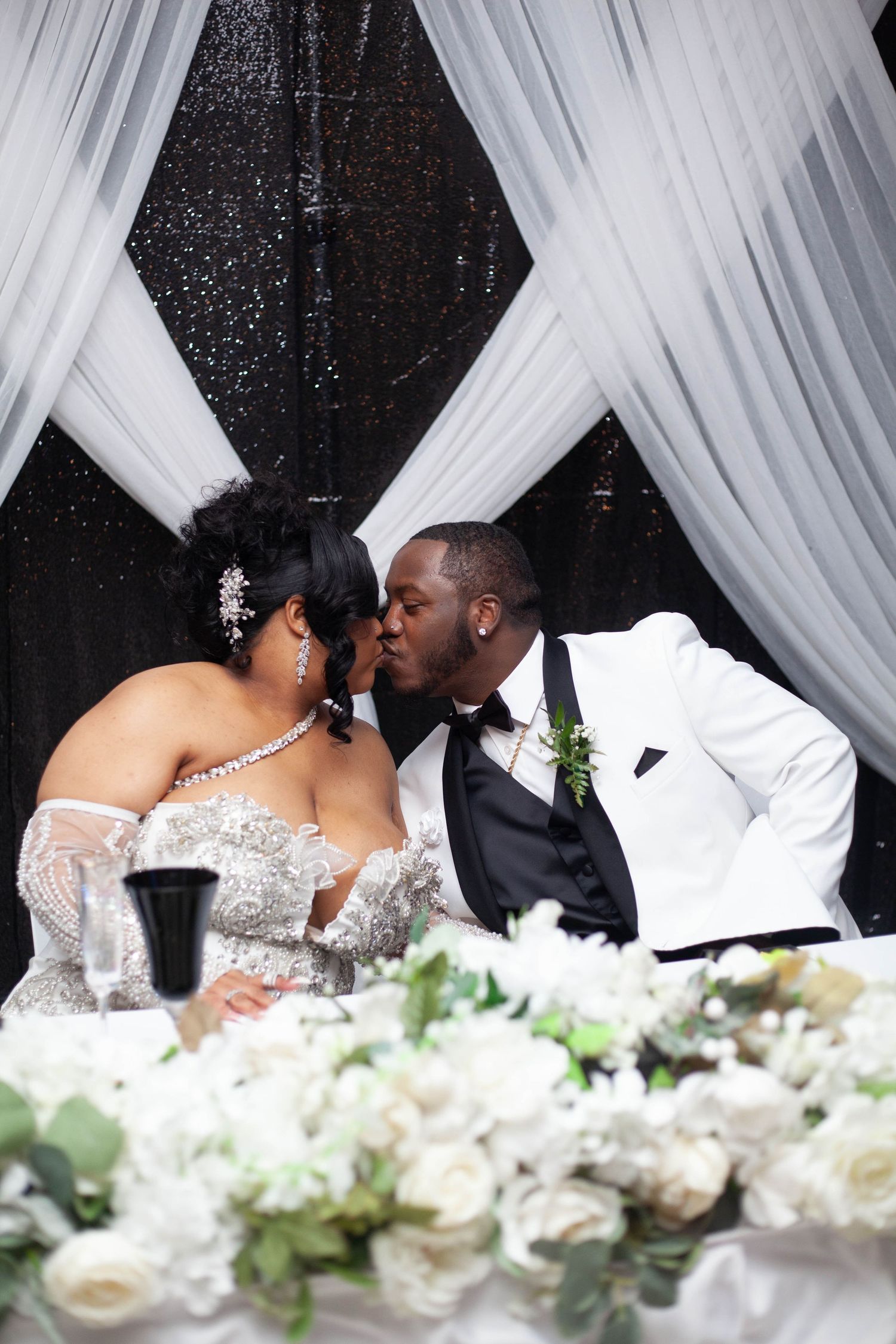 A romantic wedding moment captured through white drapes with floral decorations in the foreground.