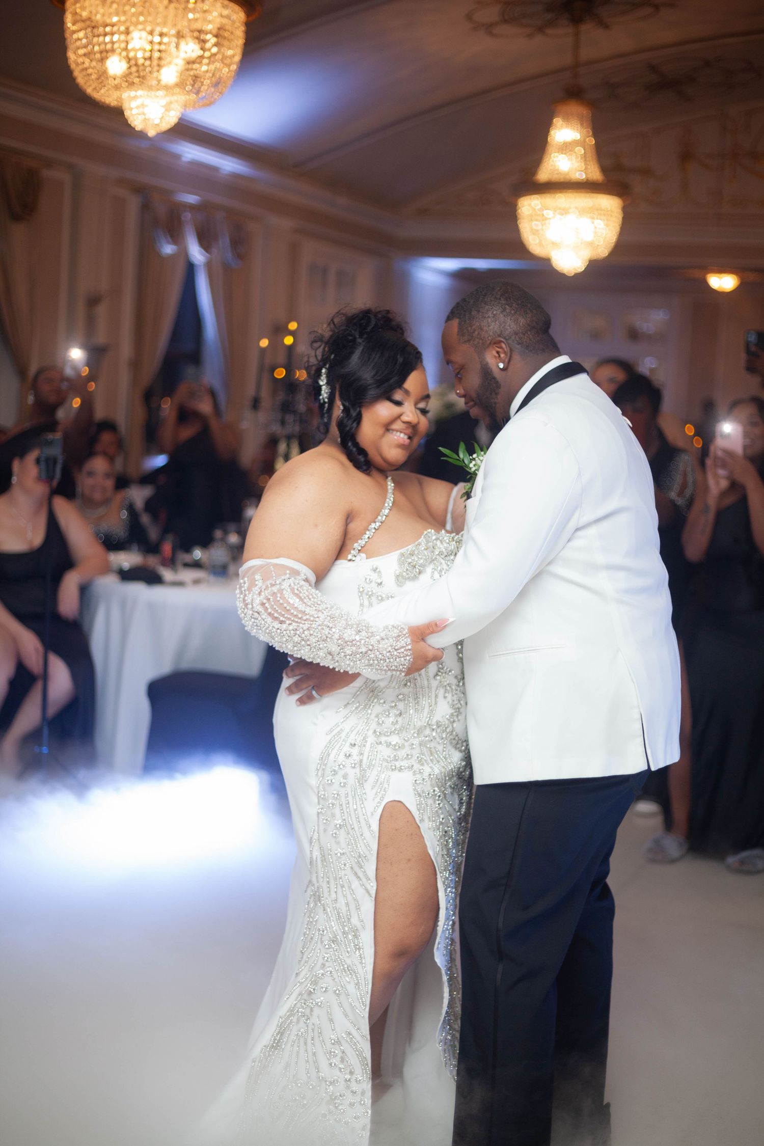 A couple shares a romantic dance at an elegant wedding reception under crystal chandeliers.