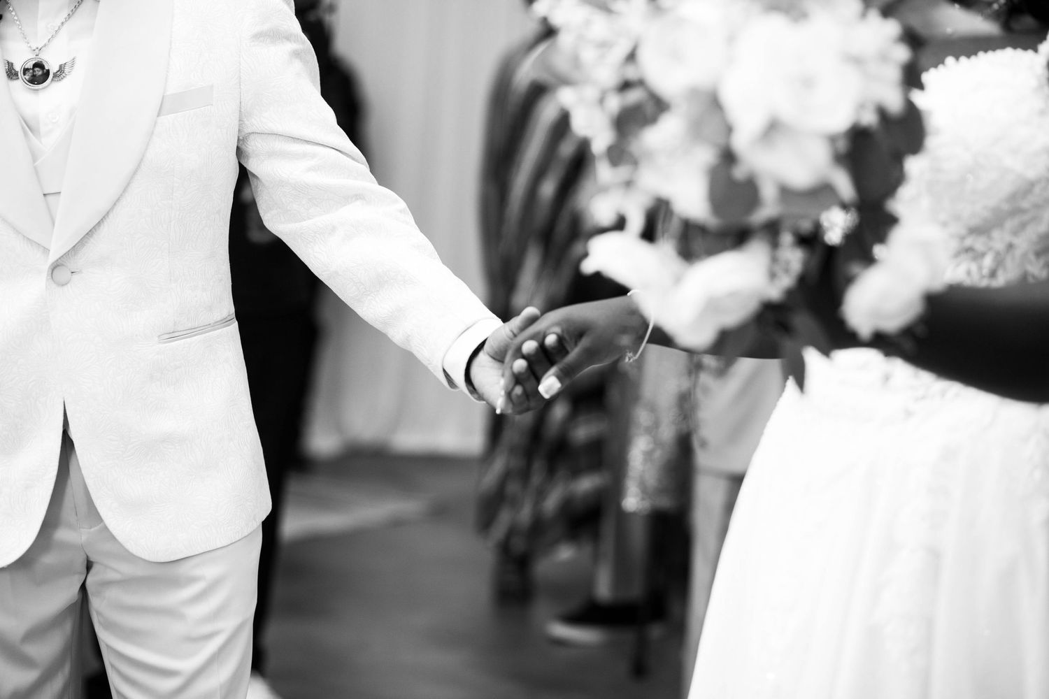 Black and white photo of a bride and groom holding hands during a wedding ceremony with bridal bouquet.