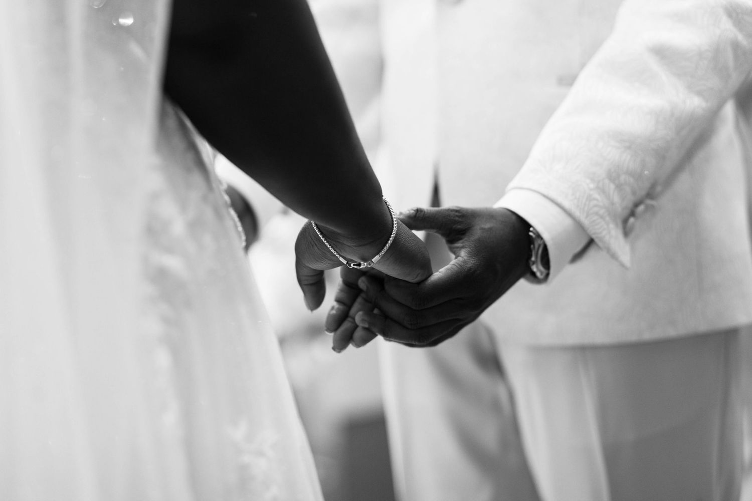 Black and white photo of a groom placing a wedding ring on the bride's finger during a wedding ceremony.