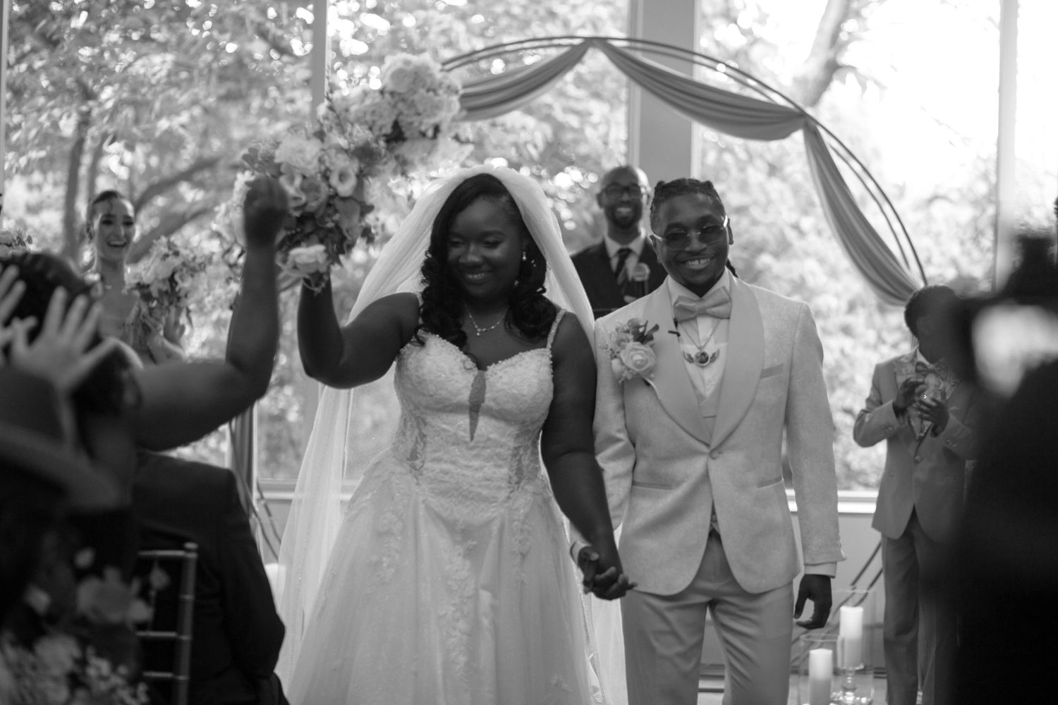 Black and white photo of a joyful bride and groom walking down the aisle after their wedding ceremony.
