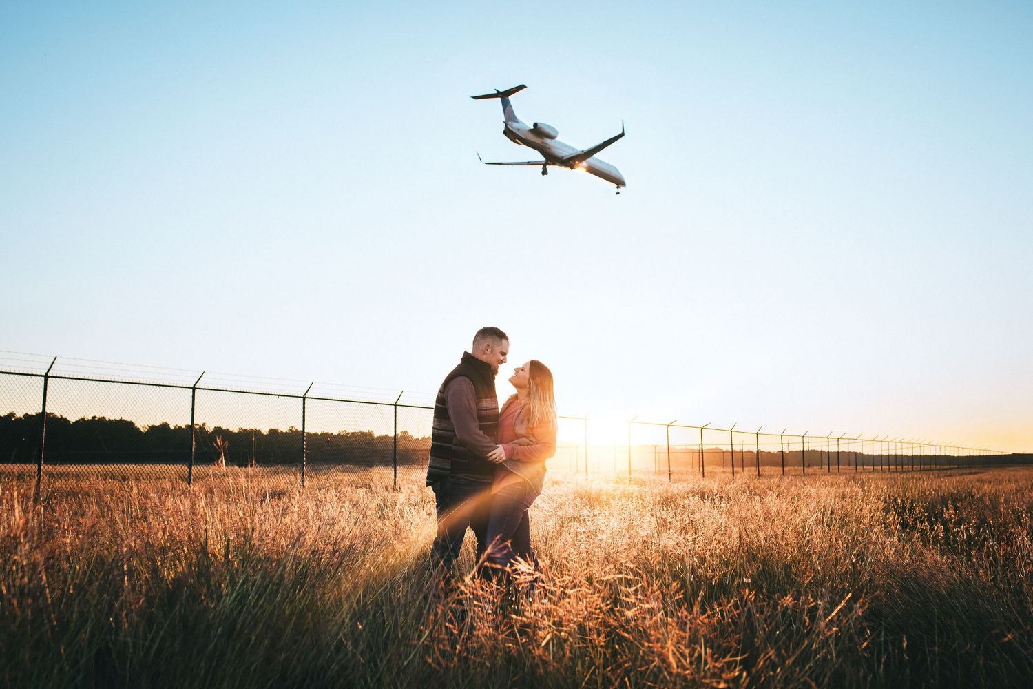 Silhouettes of people embracing in a golden wheat field at sunset with a small plane flying overhead at George Bush Intercontinental IAH