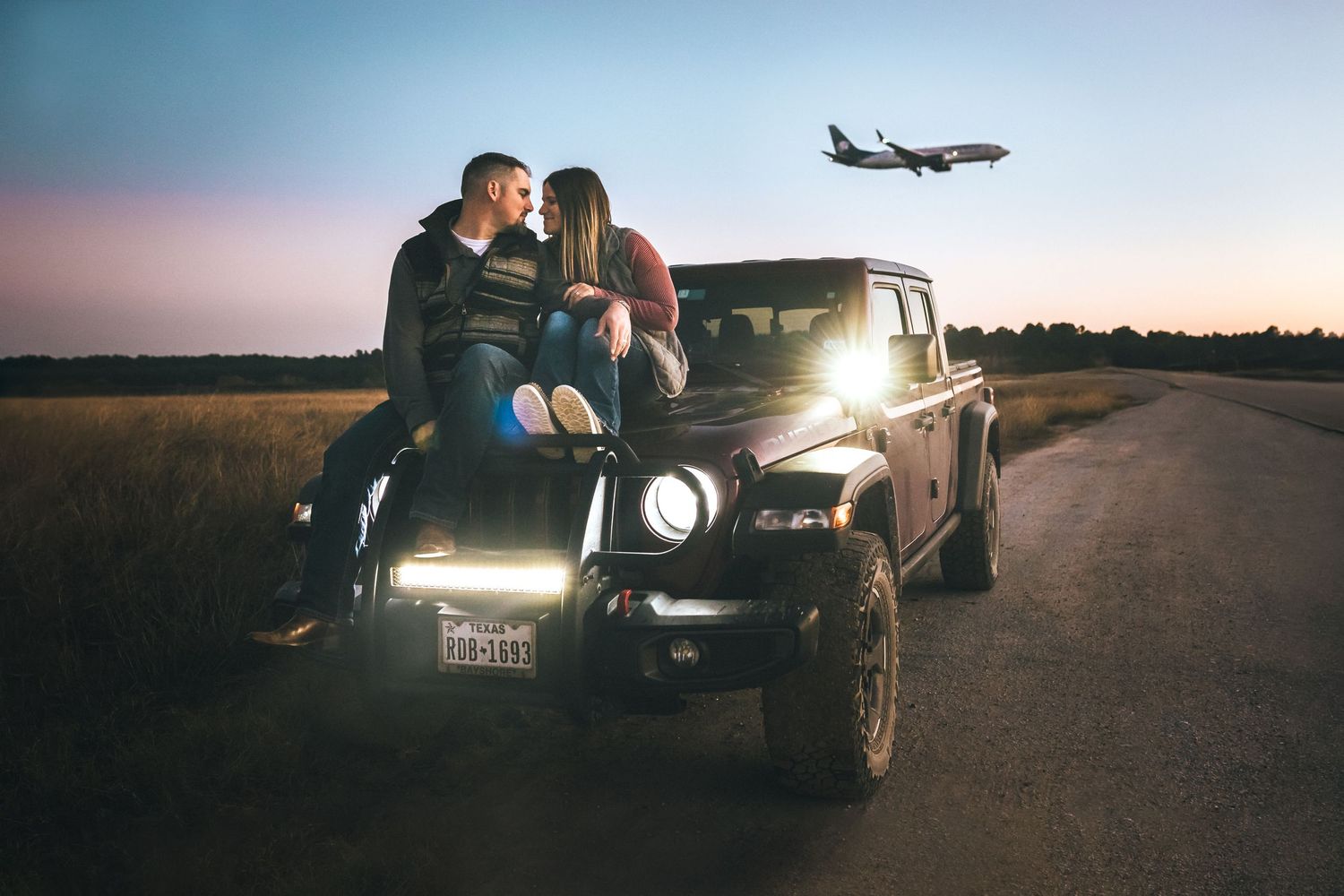A vintage black Jeep parked on a rural road at sunset with an airplane silhouetted in the sky near George Bush Intercontinental Airport.