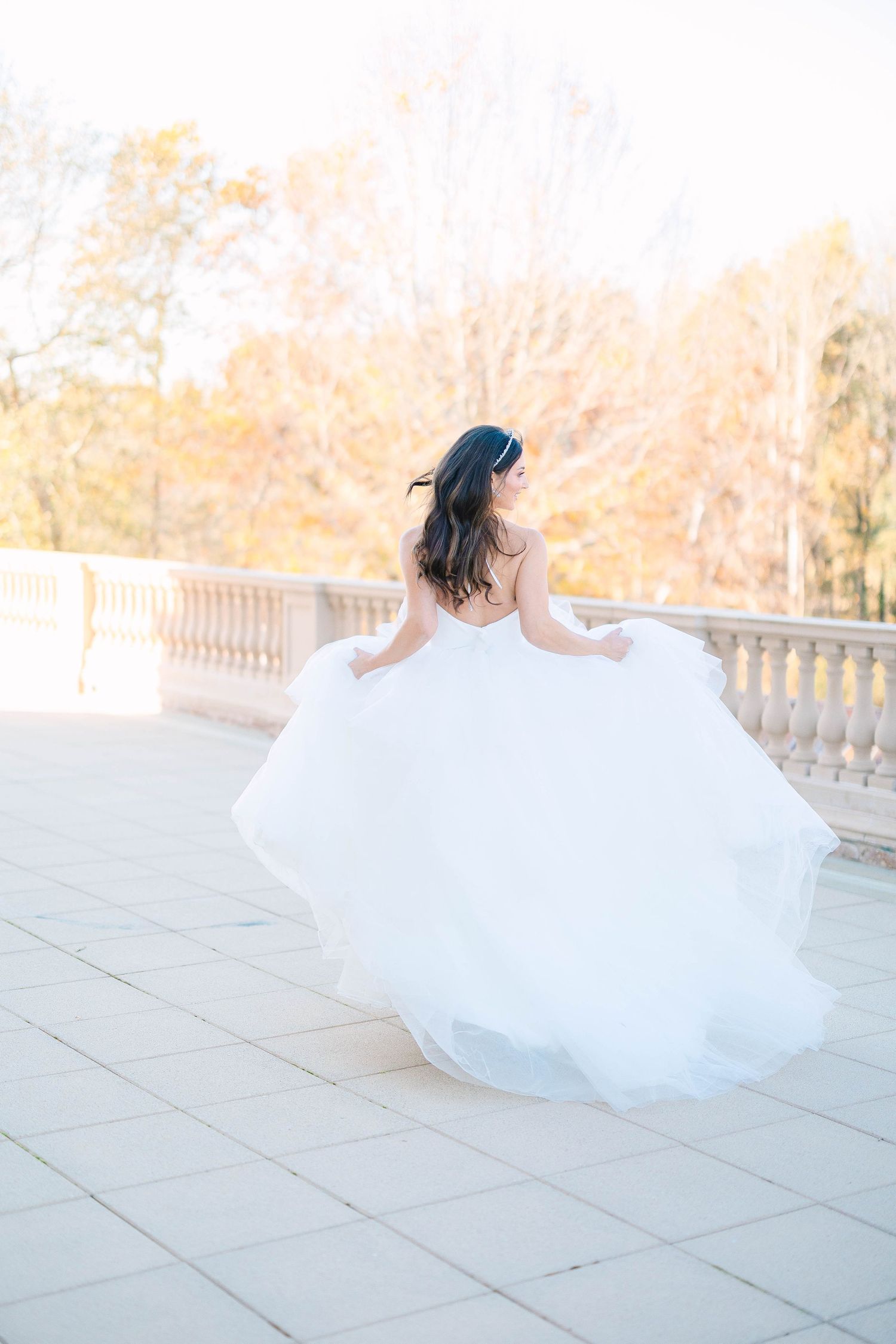 A bride in a flowing white wedding gown twirls on a stone terrace during an autumn day.