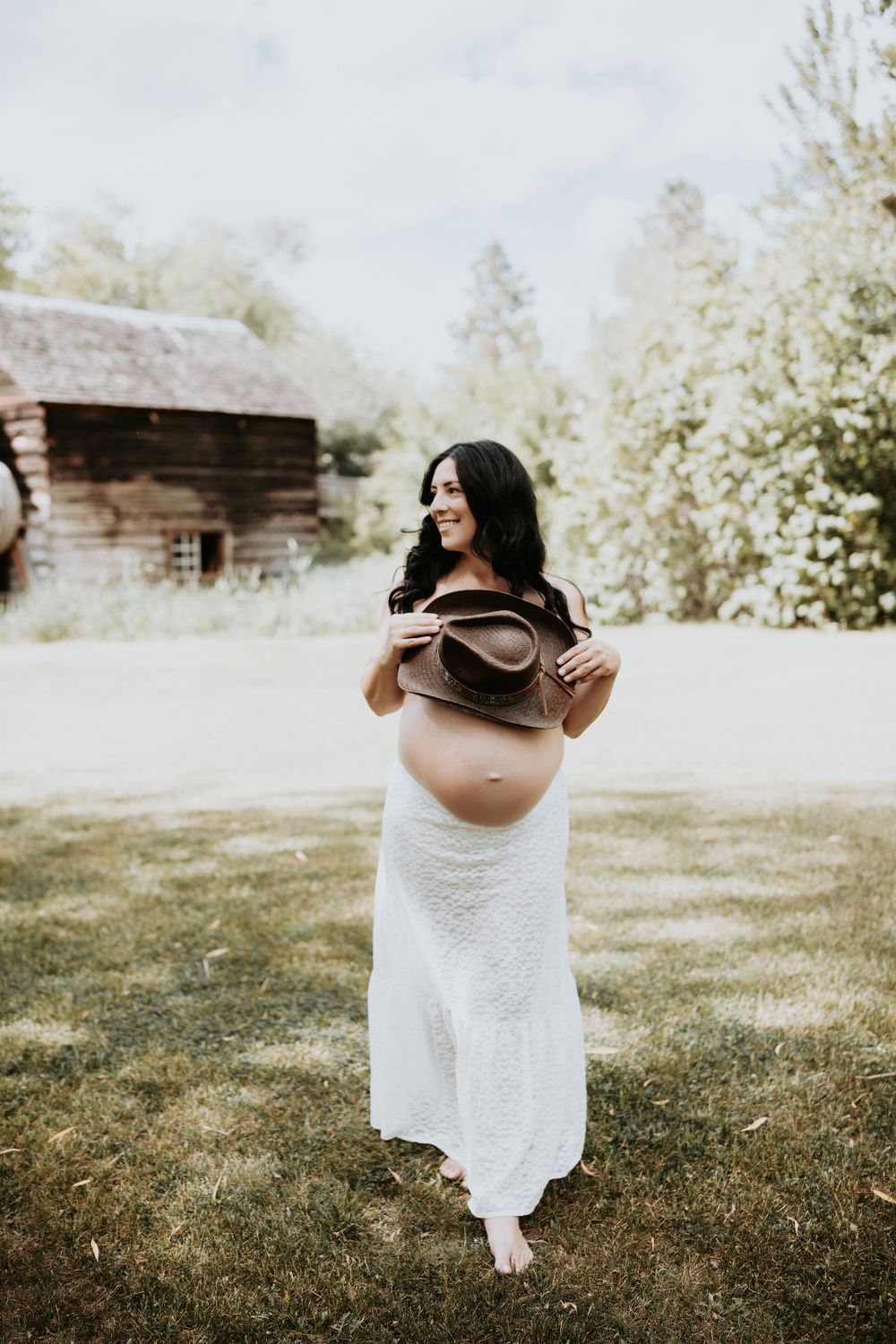 western maternity session with mama in front of barn and cowboy hat