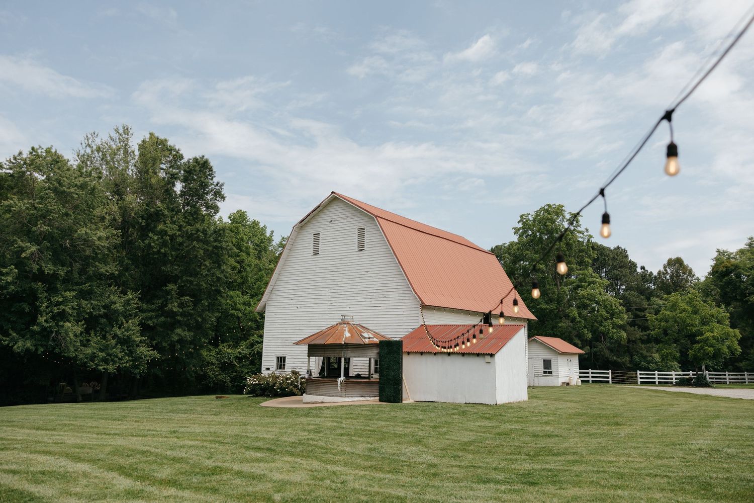 A white farmhouse with red barn and outbuildings sits on a rolling green hillside under a bright summer sky.