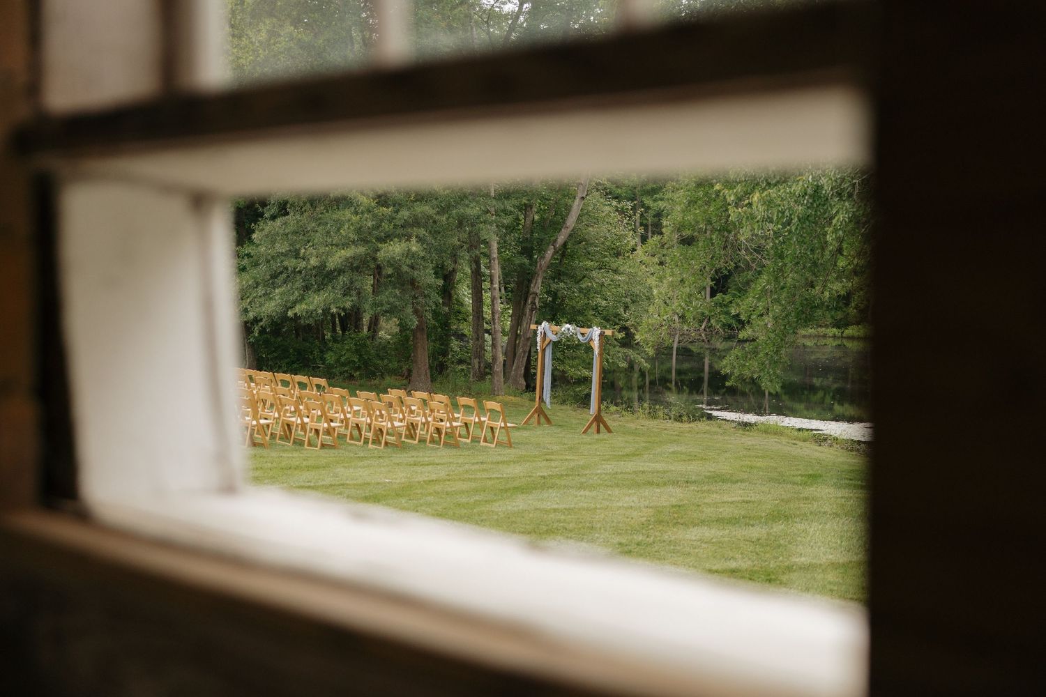 View through a window shows a green lawn and trees with stacks of firewood visible in the background.