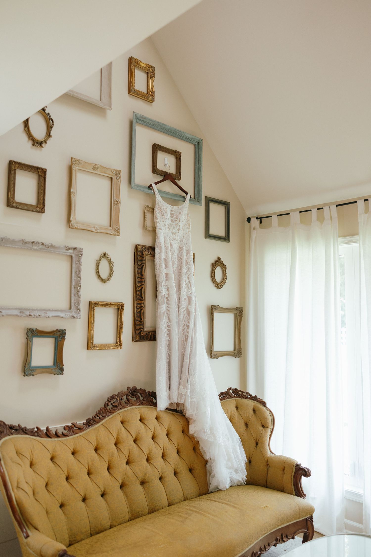 Vintage gold chaise lounge sofa with tufted upholstery against white wall decorated with empty antique picture frames.