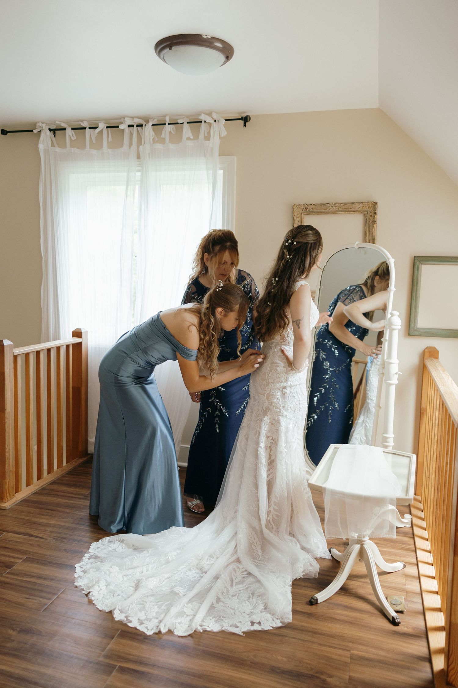 A person helps adjust the back of an elegant white lace wedding dress during a fitting session.