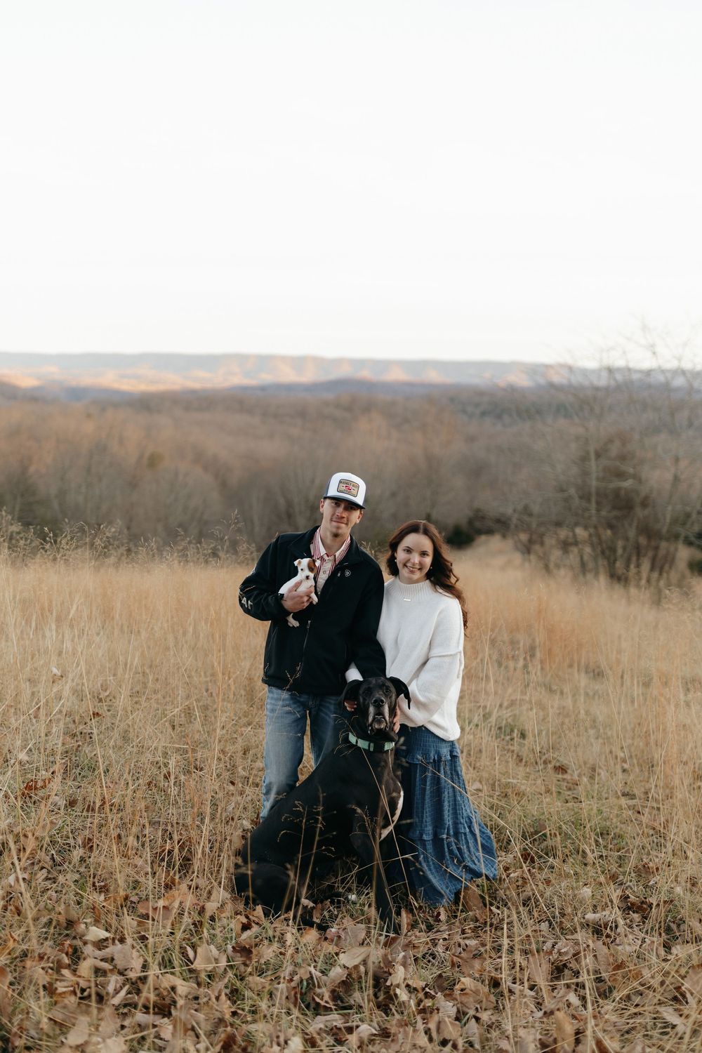 People and their black dog enjoy a heartwarming moment together in a rustic autumn field.
