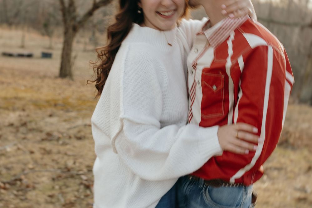A couple in white and red sweaters share affectionate moments in an outdoor autumn setting.