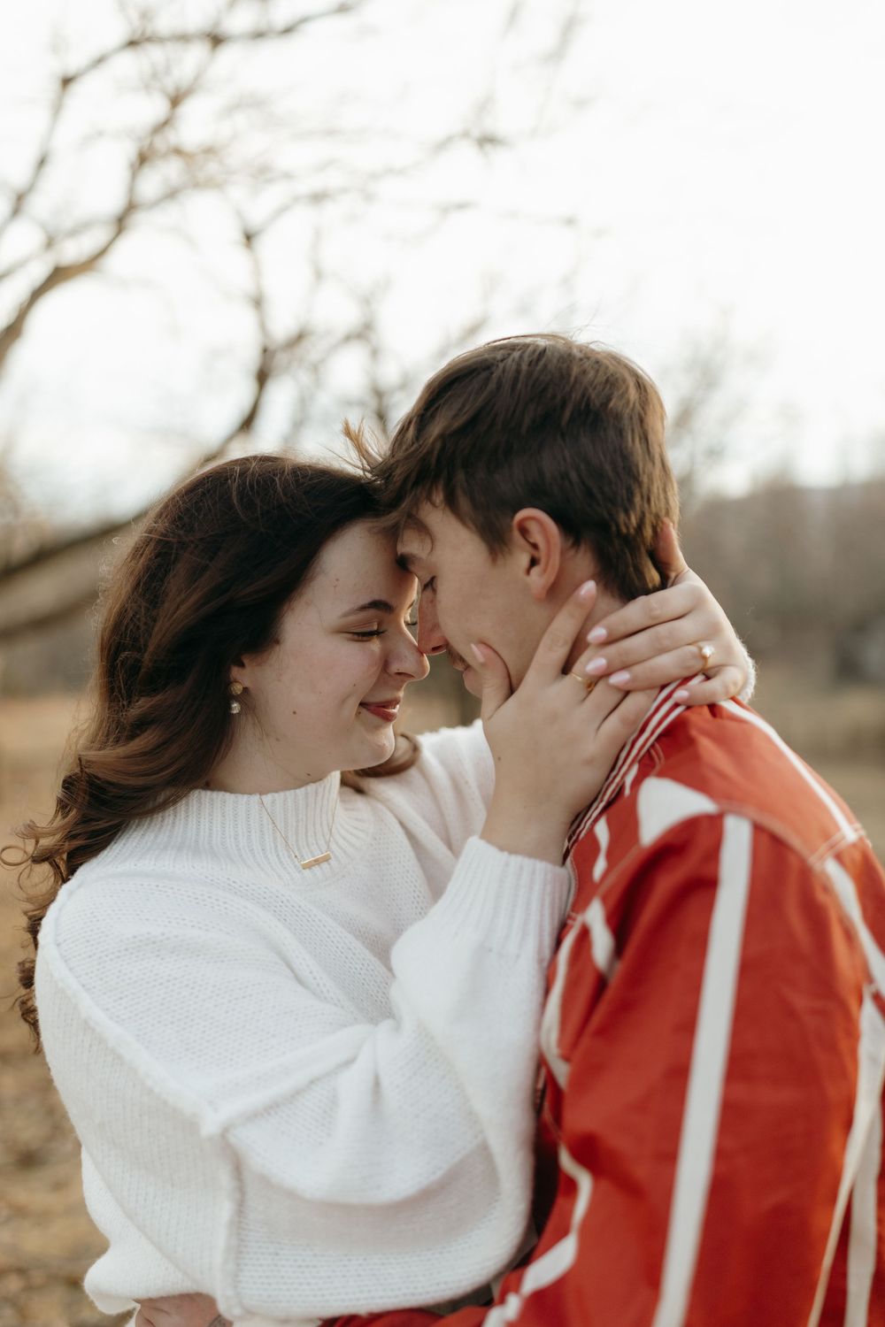 A romantic couple in white and red sweaters share tender moments together outdoors during a winter photoshoot.