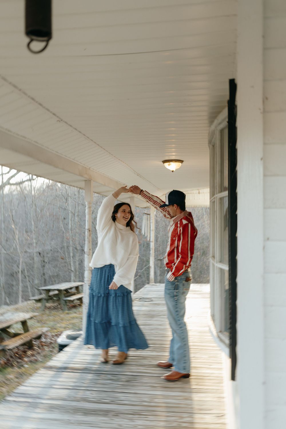 A couple dances together on a rustic white porch with bare trees in the background.