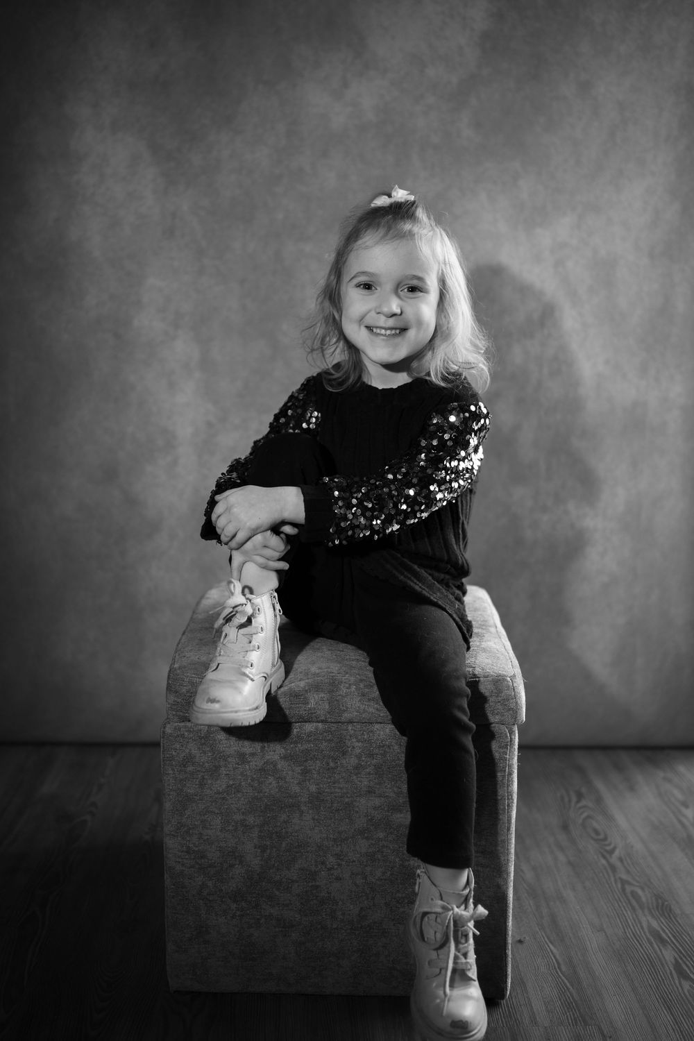 Black and white artistic portrait series showing a child in sequined outfit making playful poses on wooden floor.
