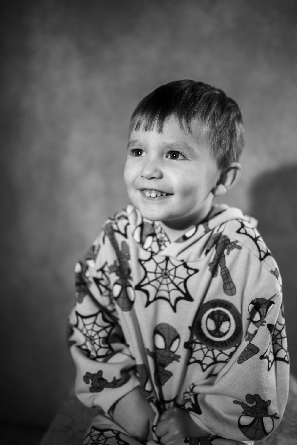 A black and white sequence of photos showing a baby in a patterned spider-themed shirt making playful expressions.