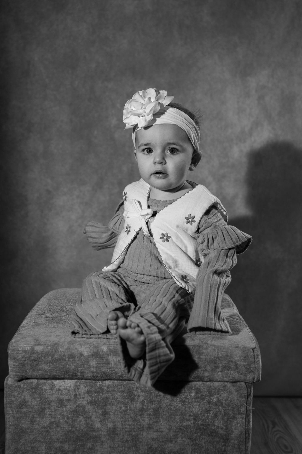 Black and white photo sequence of a baby in vintage-style dress sitting on an antique ottoman.