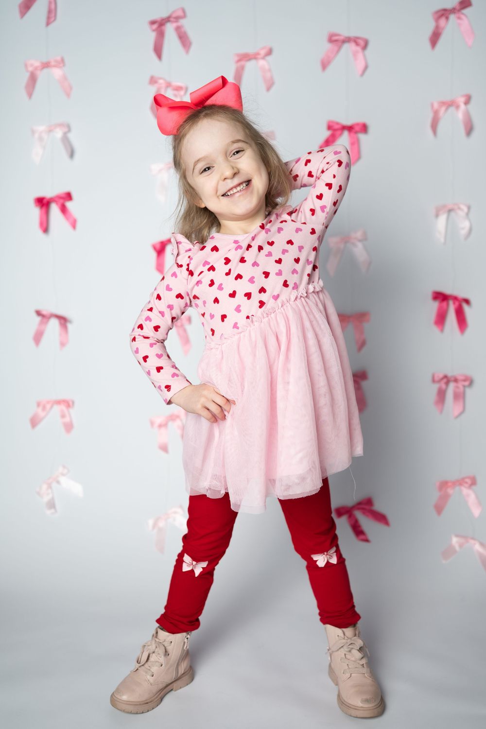 Sweet Valentine's themed photo with pink heart dress, red leggings and pink bow against bow patterned background.