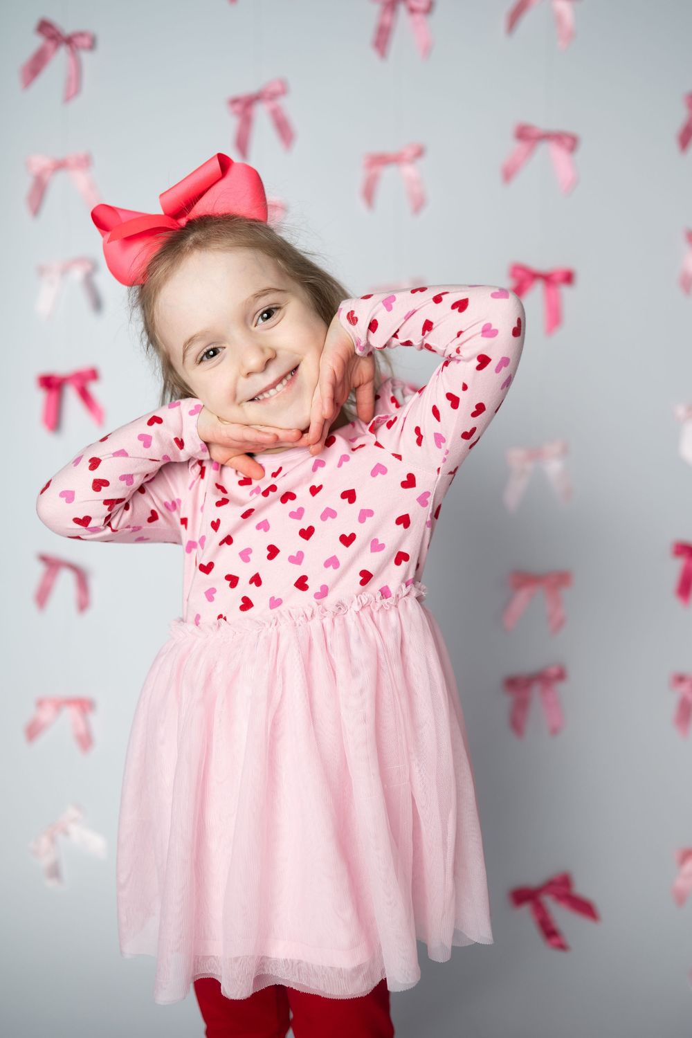 Pink and red heart-patterned dress with tulle skirt against gray background with pink bow decorations.