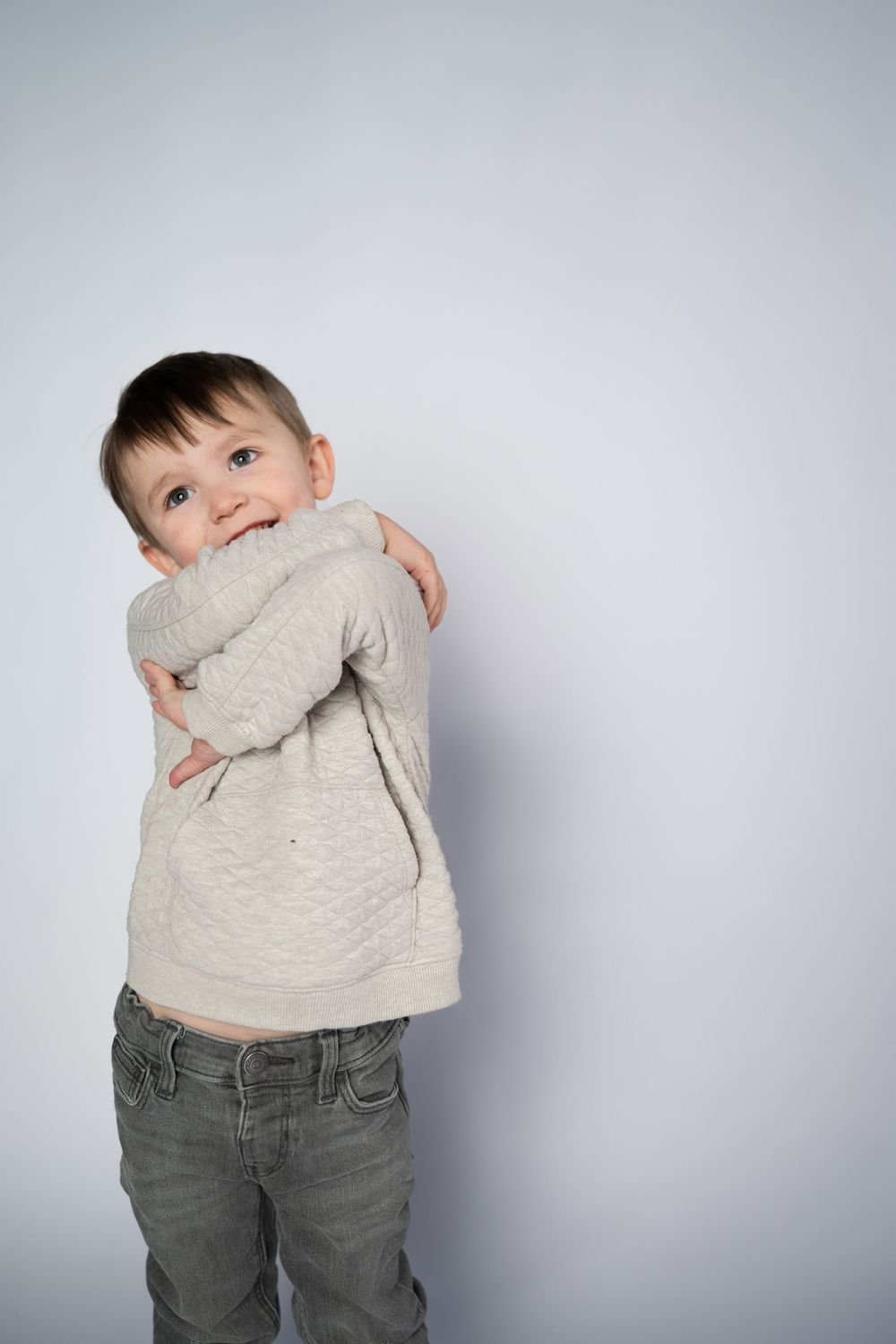 A playful child in a beige sweater and gray jeans poses against a light gray background in four sequential shots.