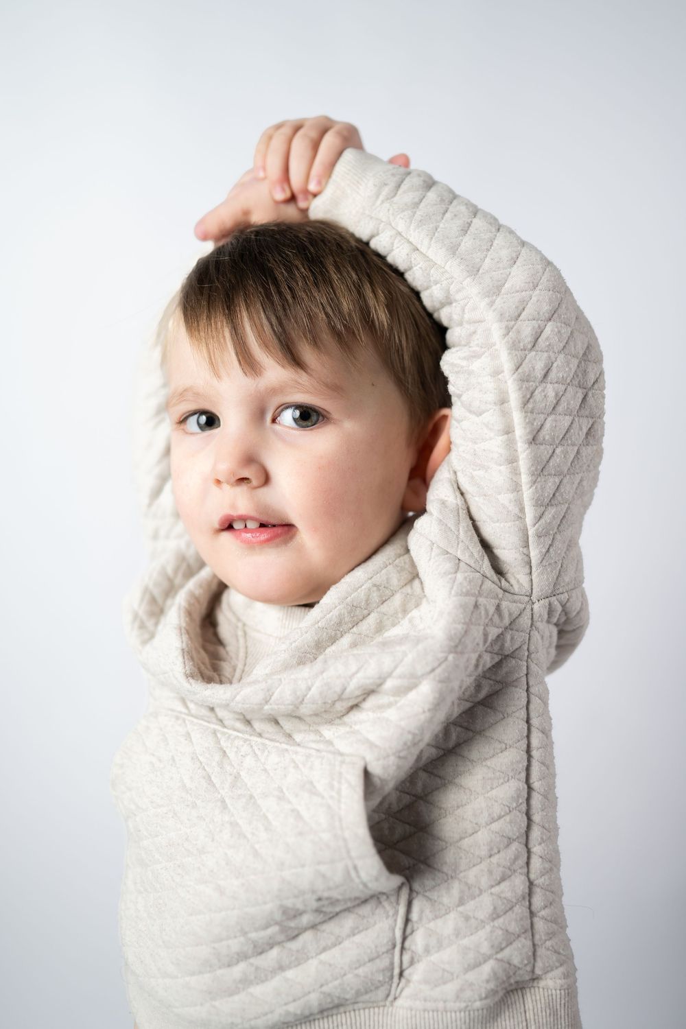 A young child wearing a cozy cream-colored quilted sweater poses against a light background.