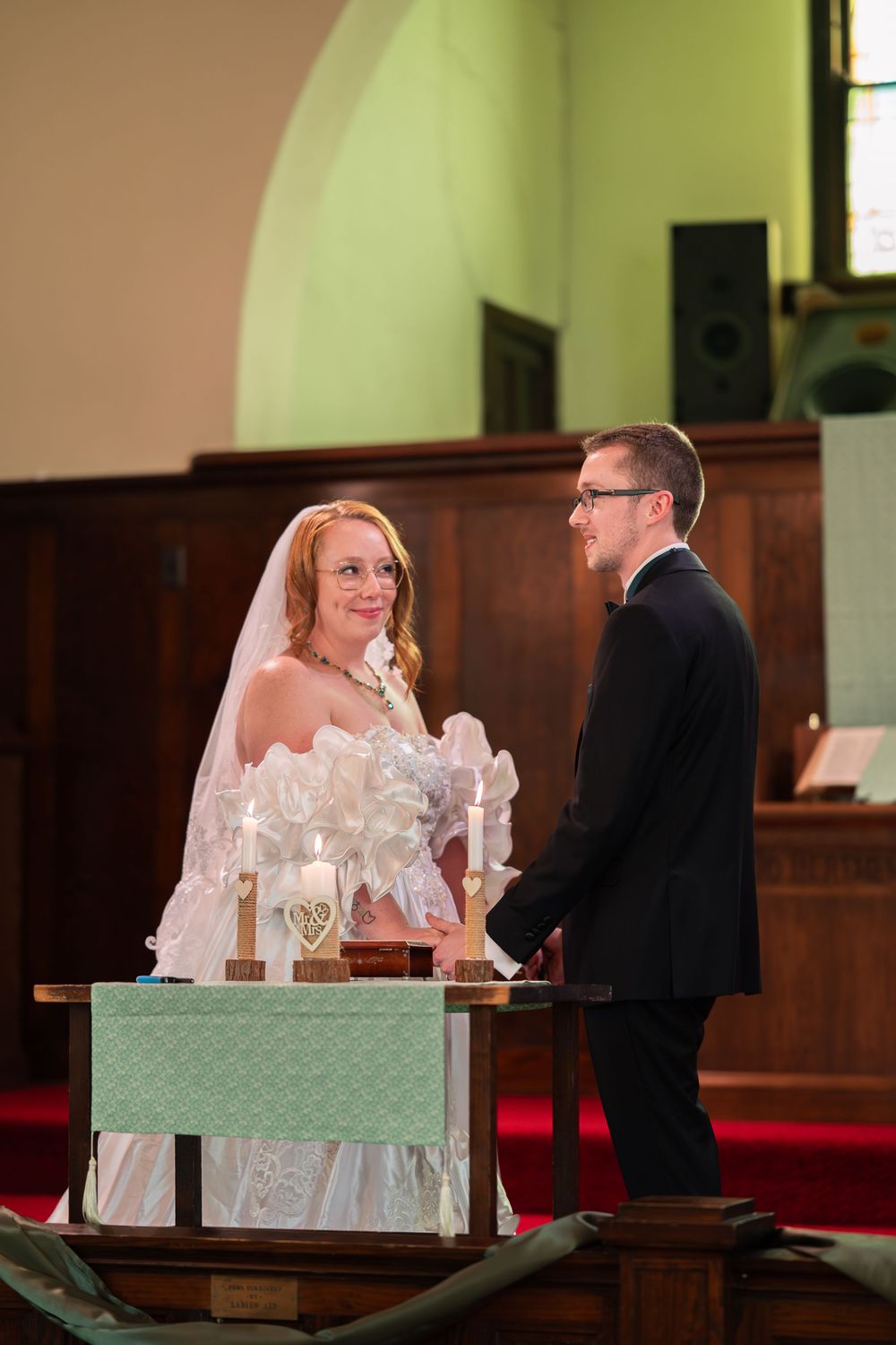 Bride and groom exchanging vows at church altar, bride in white gown and veil, groom in dark suit.