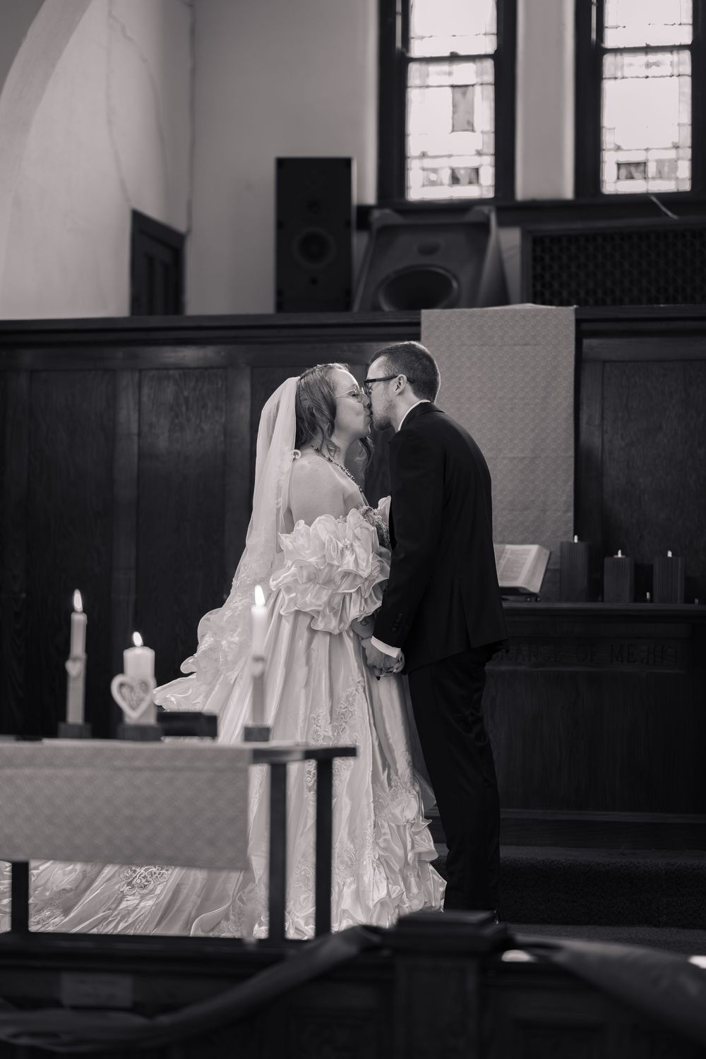 Black and white photo of a bride and groom sharing their first kiss at the altar during a church wedding ceremony.