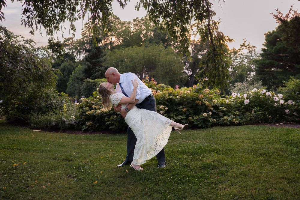 Groom dips bride in lush garden at sunset during romantic outdoor wedding photo session.