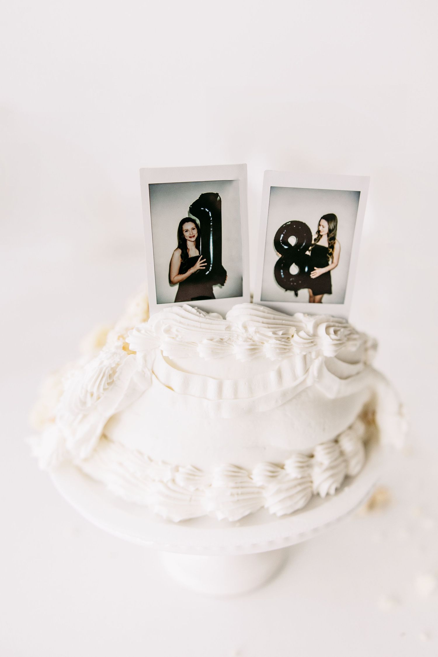 A white wedding cake decorated with ruffles displays two polaroid photos on top.