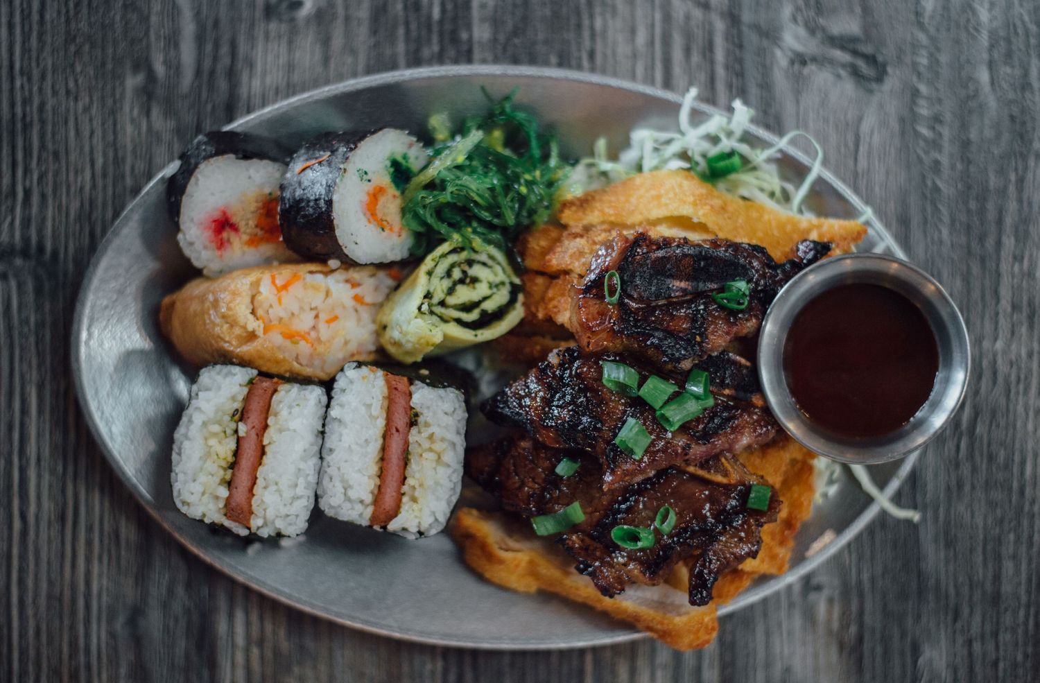Artfully plated sushi and meat dish with sauce on dark wooden surface.